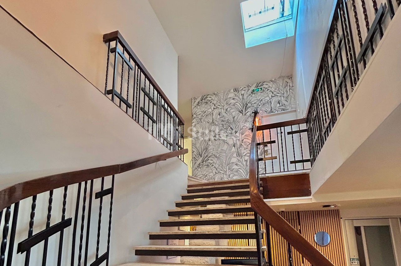Escalier intérieur en bois et métal avec mur décoré de motifs végétaux et puits de lumière au plafond.
