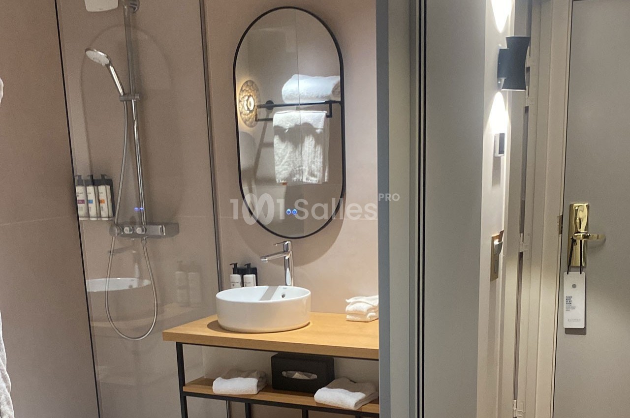 Salle de bain moderne avec douche à l'italienne, miroir ovale, lavabo sur meuble en bois et serviettes pliées.
