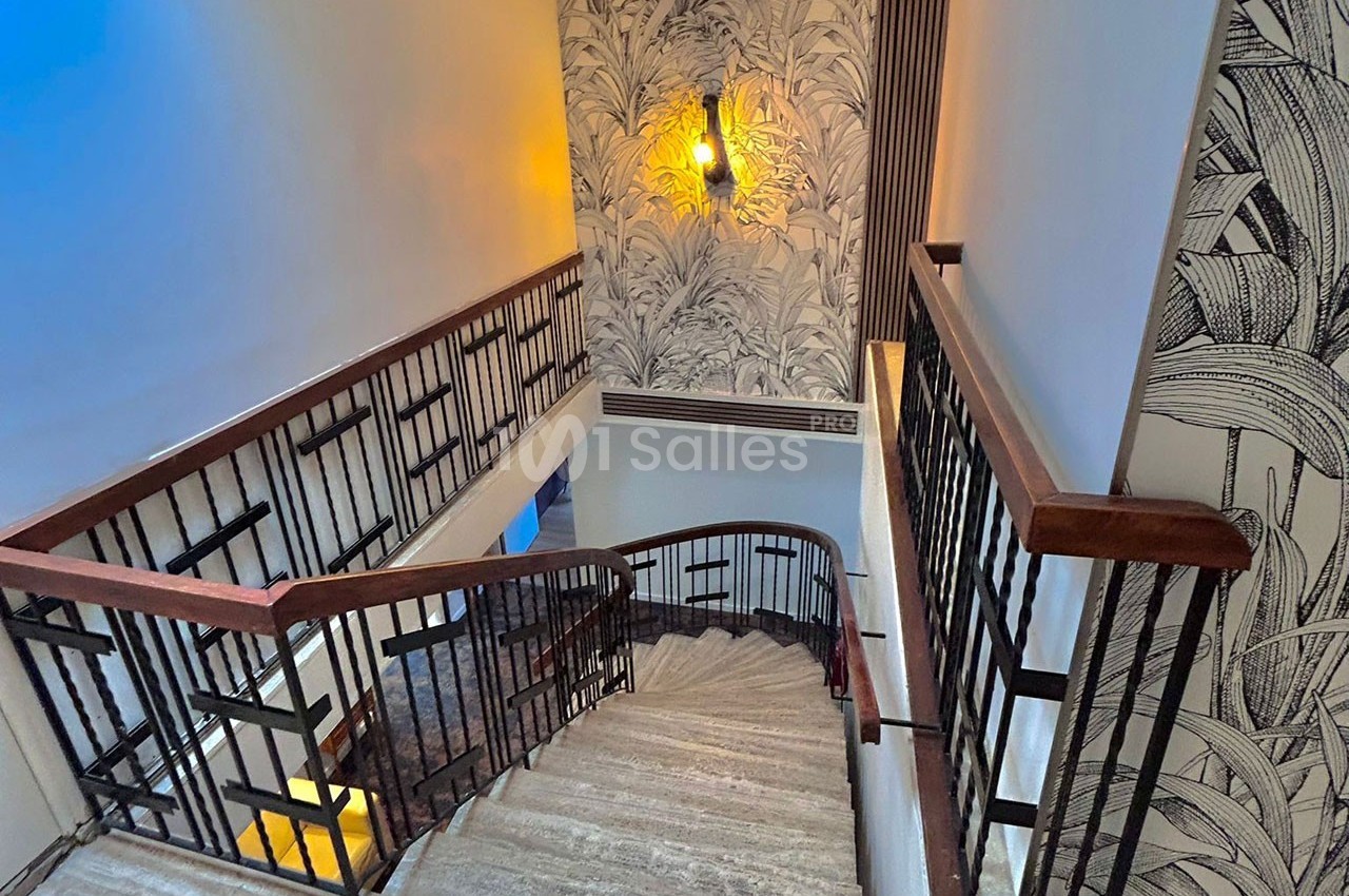 Escalier intérieur en bois et métal avec murs décorés de motifs végétaux et éclairage mural chaleureux.