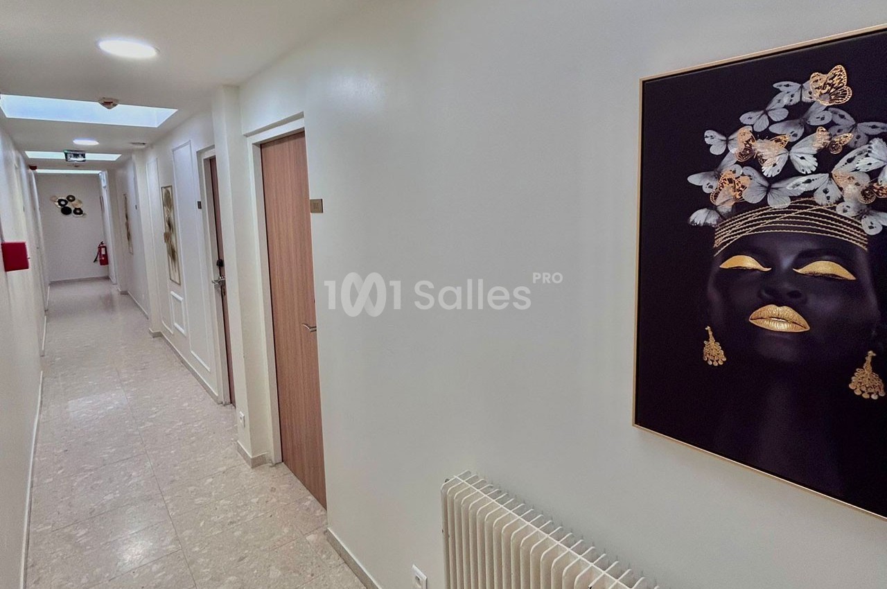 Couloir lumineux avec murs blancs, portes en bois, tableau représentant un visage décoré de papillons et éléments dorés.