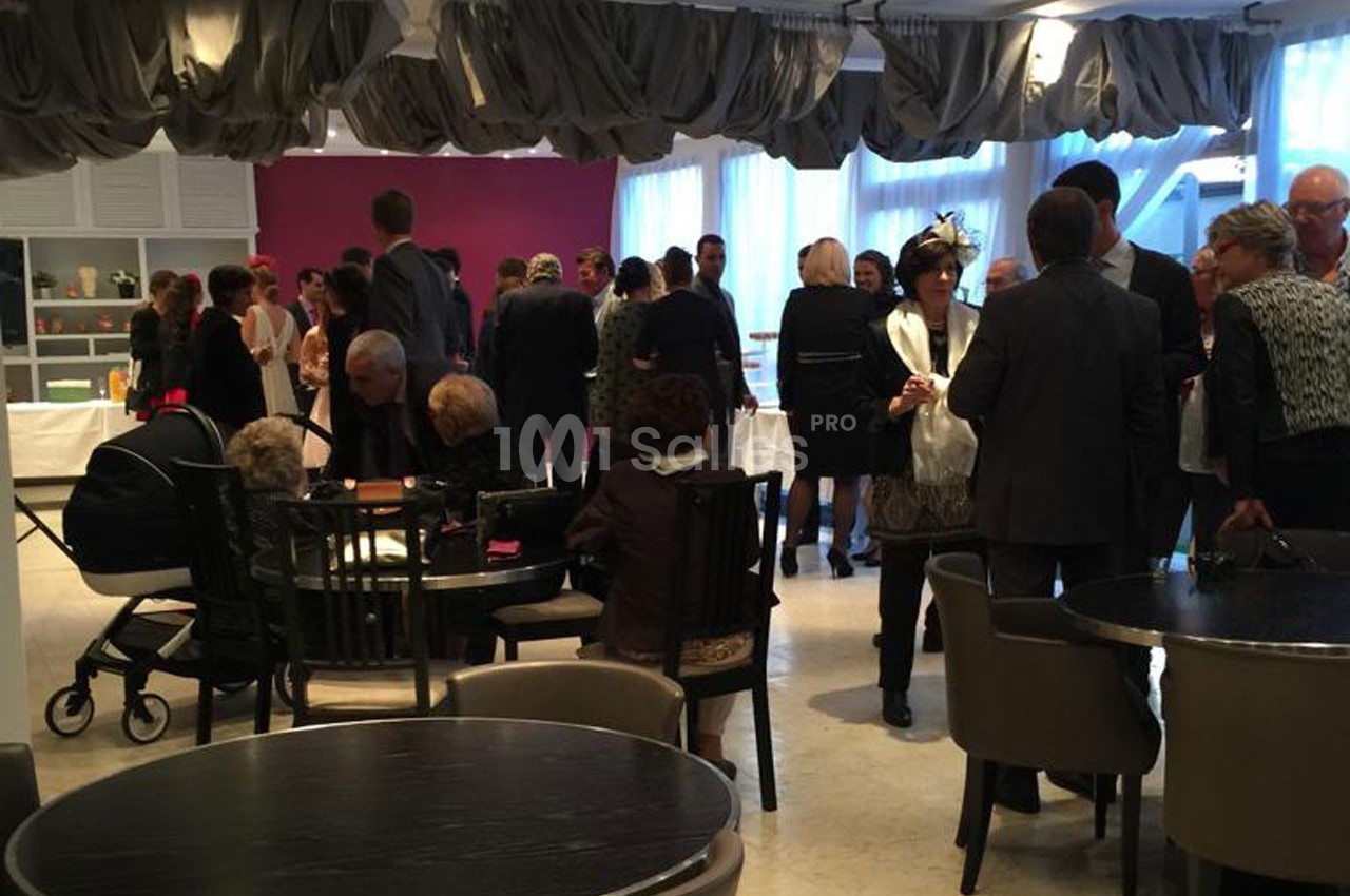 Groupe de personnes debout et assises dans une salle de réception éclairée, discutant autour de tables.