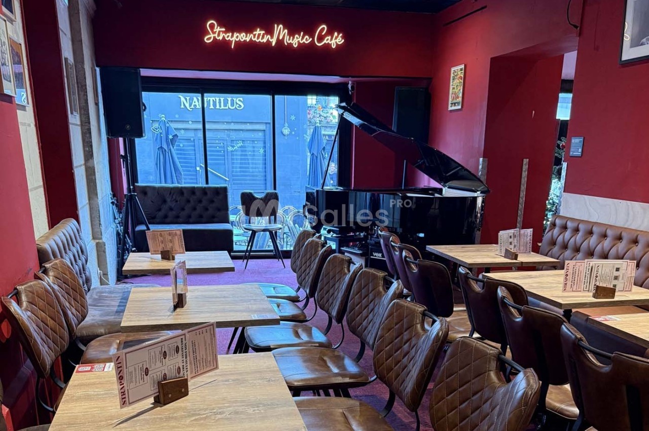 Salle de café avec des tables en bois, des chaises rembourrées et un piano à queue noir près d'une baie vitrée.