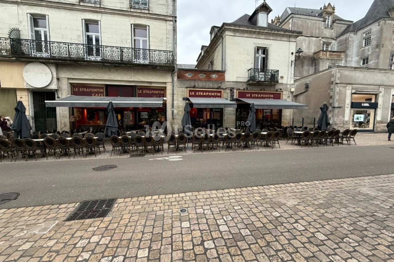 Façade d'un café avec terrasse vide, rangée de chaises et tables alignées, située dans une rue pavée.