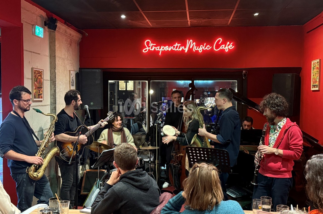 Groupe de musiciens jouant en live dans un café à l'ambiance chaleureuse, devant un public attentif.
