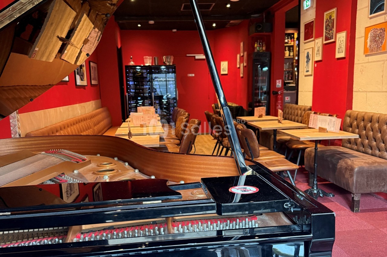 Vue d'un piano à queue dans un restaurant à la décoration chaleureuse avec murs rouges et tables alignées.
