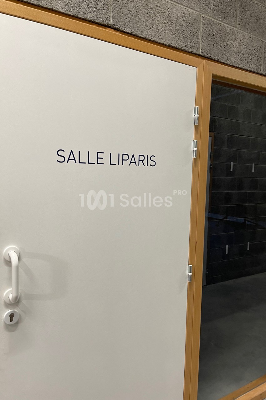 Porte blanche avec l'inscription ’Salle Liparis’, entourée d'un cadre en bois et située dans un mur en béton.