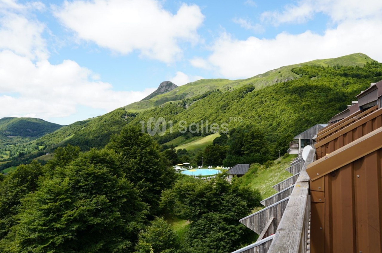 Vue sur des collines verdoyantes avec une piscine entourée d'arbres, prise depuis un balcon en bois.