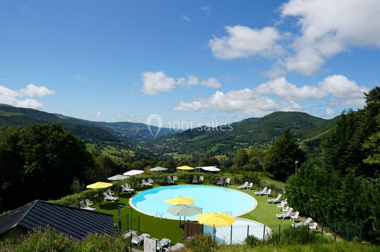 Piscine extérieure entourée de chaises longues et parasols jaunes, avec vue sur des collines verdoyantes sous un ciel bleu.