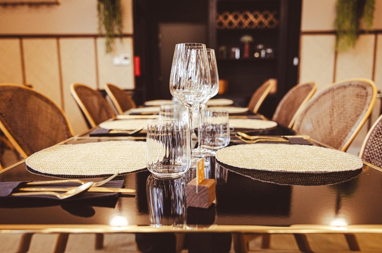 Table dressée avec des assiettes en osier, des verres en cristal, des couverts dorés et des serviettes noires.