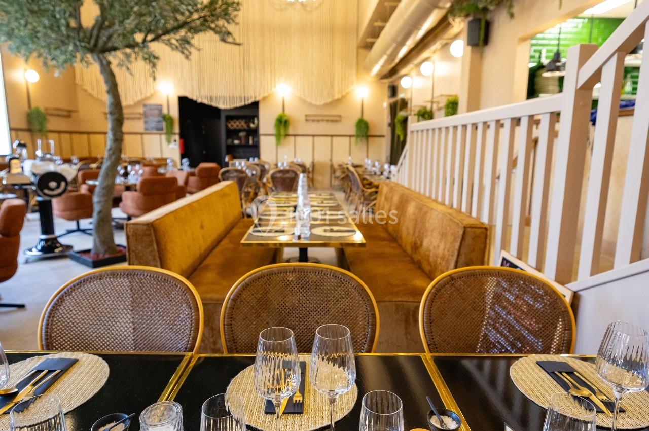 Salle de restaurant moderne avec tables dressées, chaises en rotin, banquettes et décoration végétale.