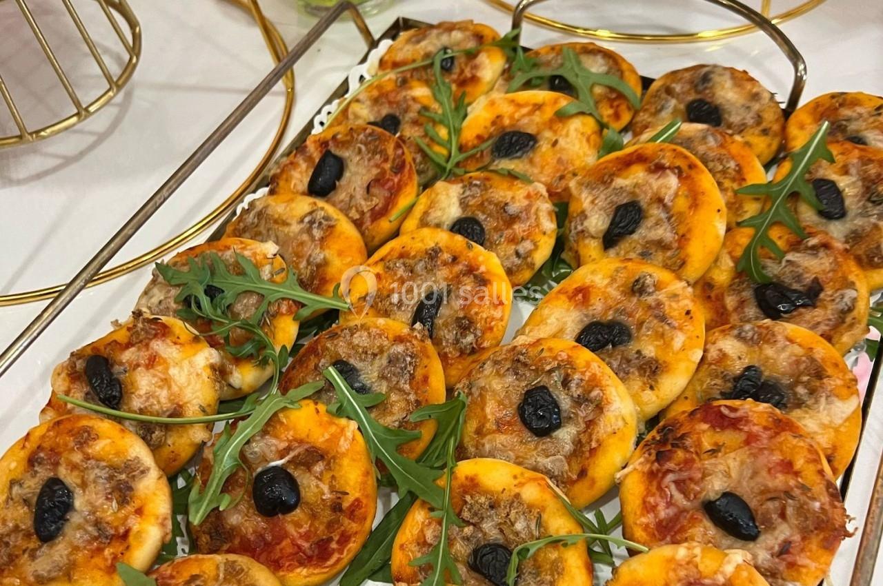 Plateau de mini-pizzas garnies de fromage, olives noires, viande hachée et décorées de feuilles de roquette.