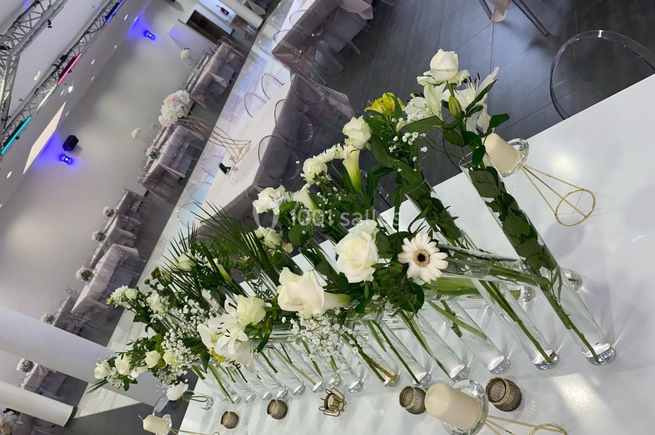 Décoration de table avec des vases alignés contenant des fleurs blanches et vertes dans une salle de réception.