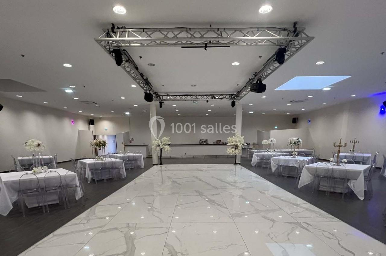 Salle de réception moderne avec sol en marbre, tables décorées de nappes blanches et éclairage suspendu.