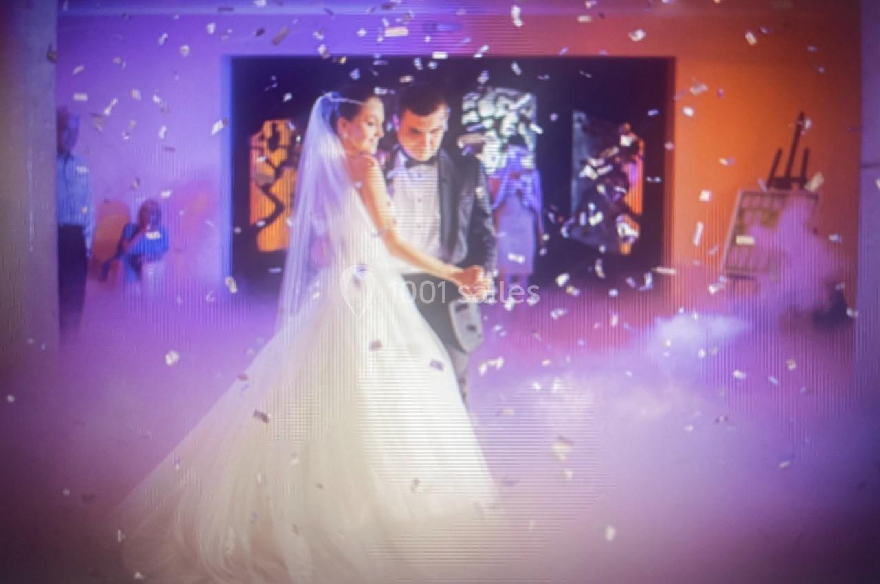 Un couple de mariés danse dans une salle décorée, entouré de fumée et de confettis.
