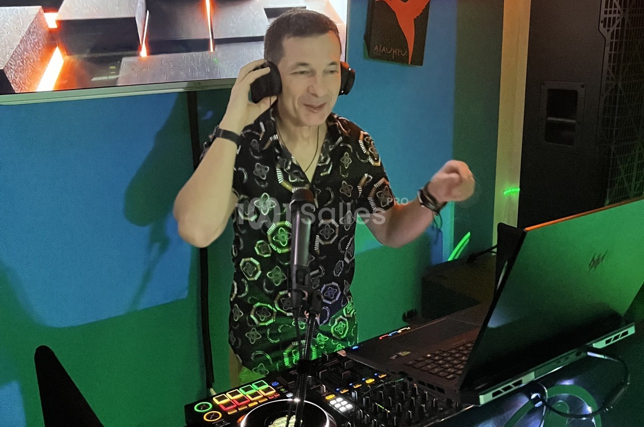 Un DJ souriant mixe de la musique sur une console dans un environnement lumineux et coloré.