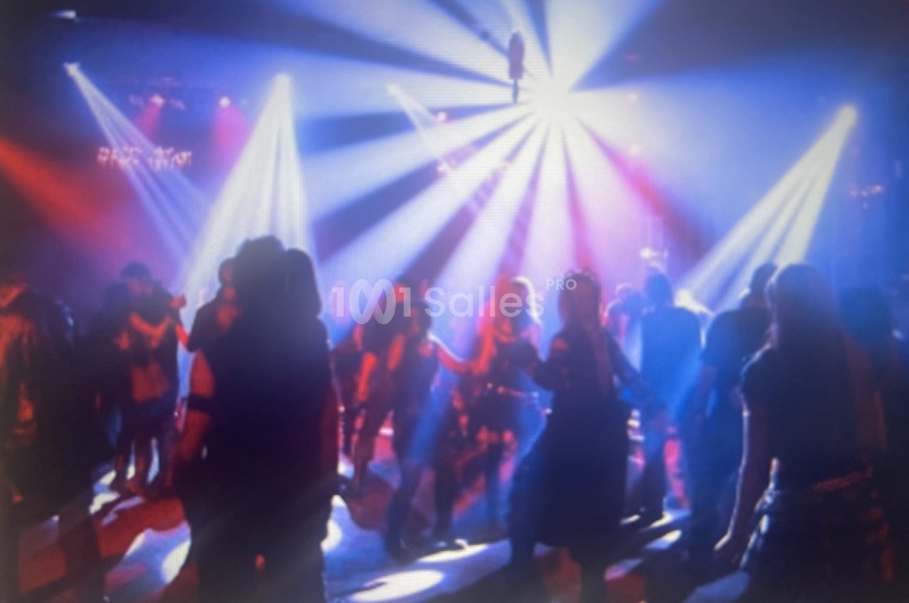 Personnes dansant dans une salle sombre éclairée par des projecteurs colorés et des faisceaux lumineux.