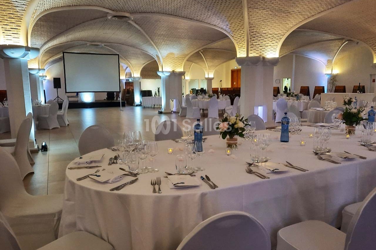Salle de réception élégante avec tables dressées, décorations florales et écran de projection en arrière-plan.