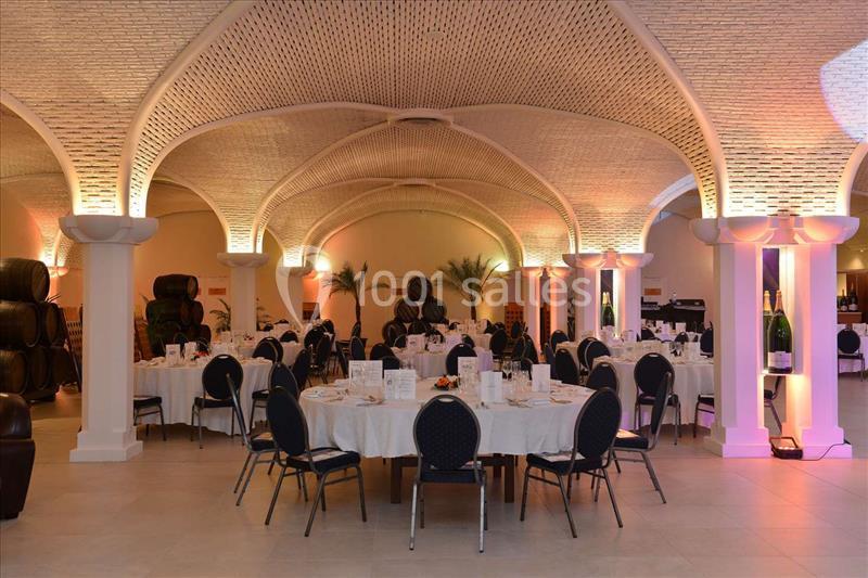 Salle voûtée élégante avec tables rondes dressées pour un événement, éclairage chaleureux et décorations sobres.