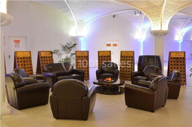 Cinq fauteuils en cuir disposés autour d'une table basse dans une salle voûtée avec des présentoirs en bois.