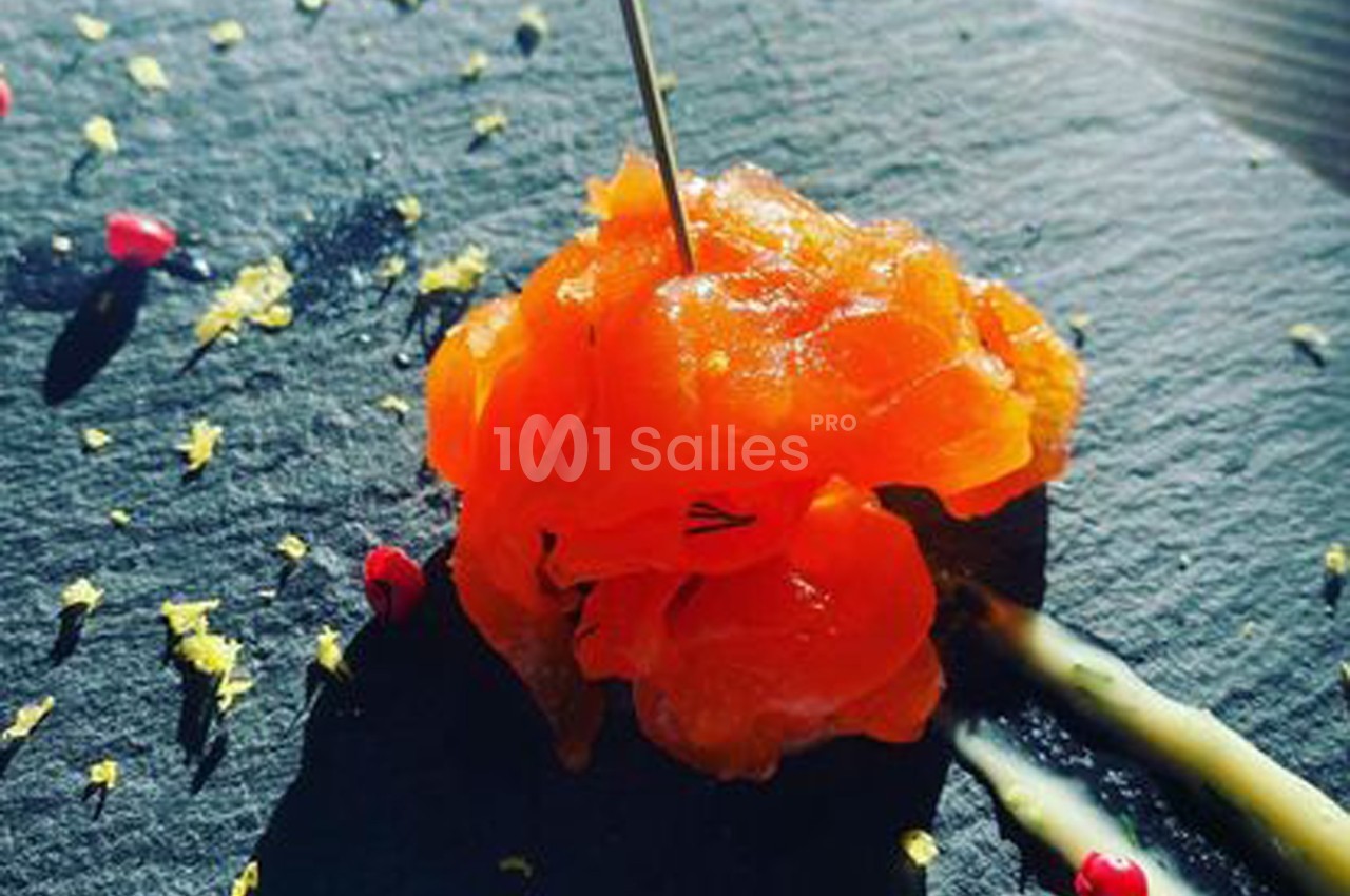 Tranche de saumon fumé sur une ardoise, décorée de zestes de citron, baies roses et filet de sauce.