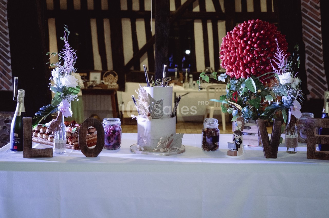 Table décorée pour un mariage avec un gâteau central, fleurs, bocaux, bouteilles et lettres formant le mot ’LOVE’.