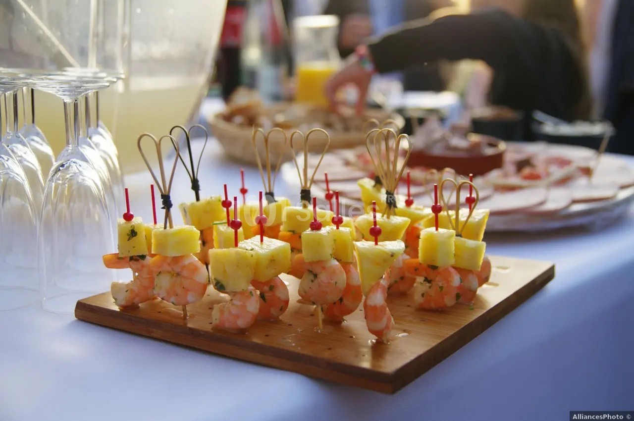 Brochettes apéritives composées de crevettes et morceaux d'ananas, présentées sur une planche en bois.