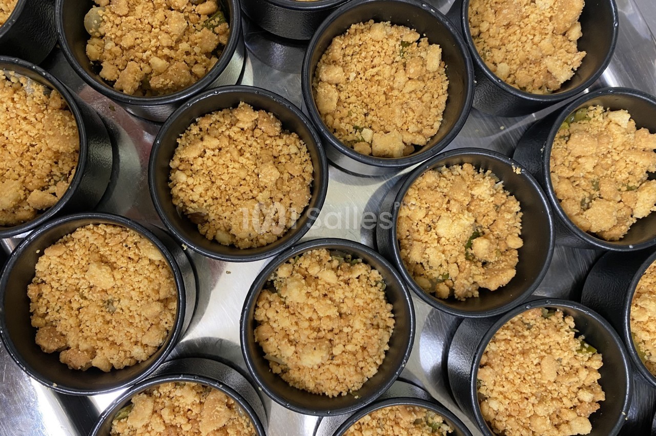 Desserts individuels au crumble doré, présentés dans des ramequins noirs sur une surface métallique.