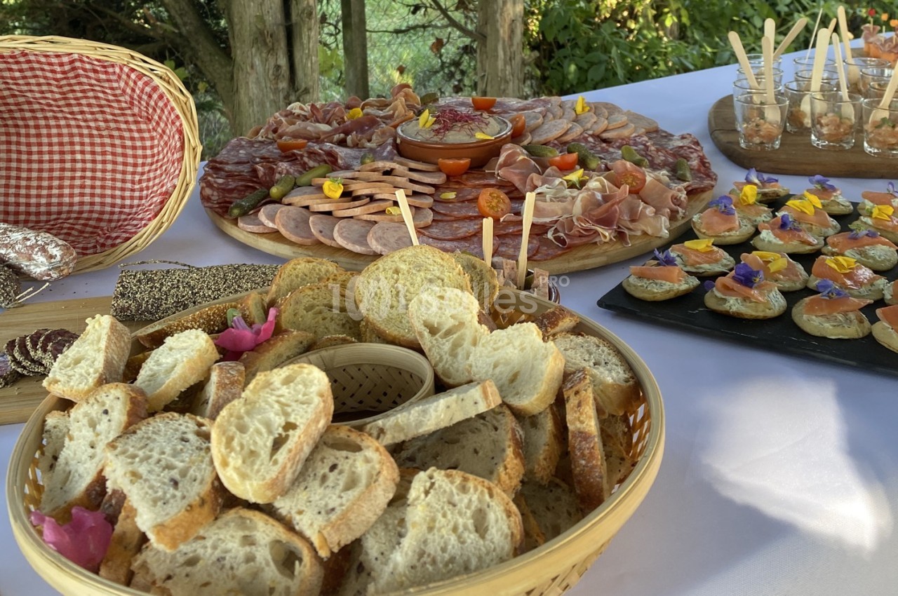 Plateau de pain tranché, charcuteries, verrines et toasts disposés sur une table pour un buffet en extérieur.