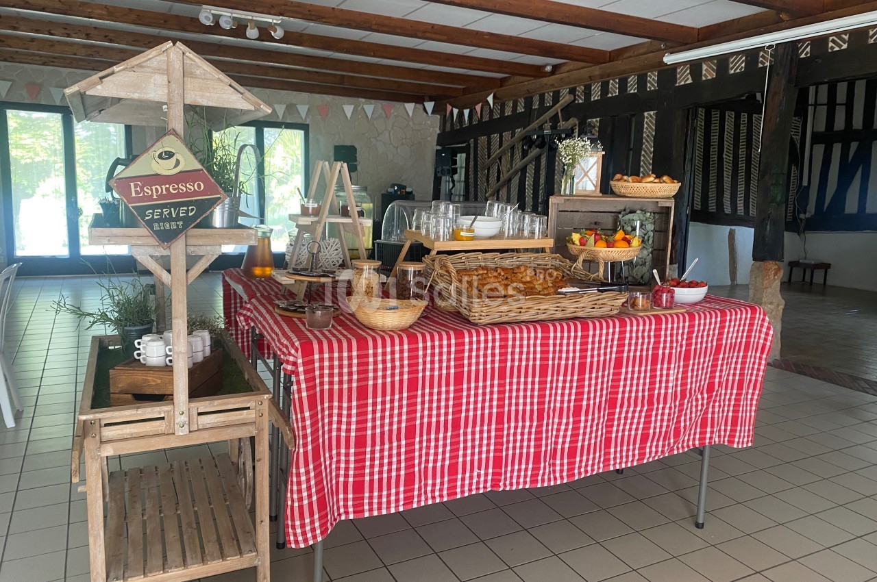 Buffet avec viennoiseries, fruits, jus et café, disposé sur une table recouverte d'une nappe rouge à carreaux.