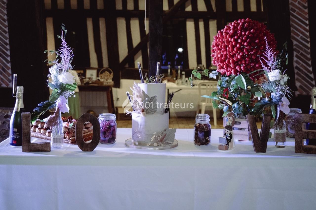 Table décorée pour un mariage avec un gâteau central, fleurs, bocaux, bouteilles et lettres formant le mot ’LOVE’.