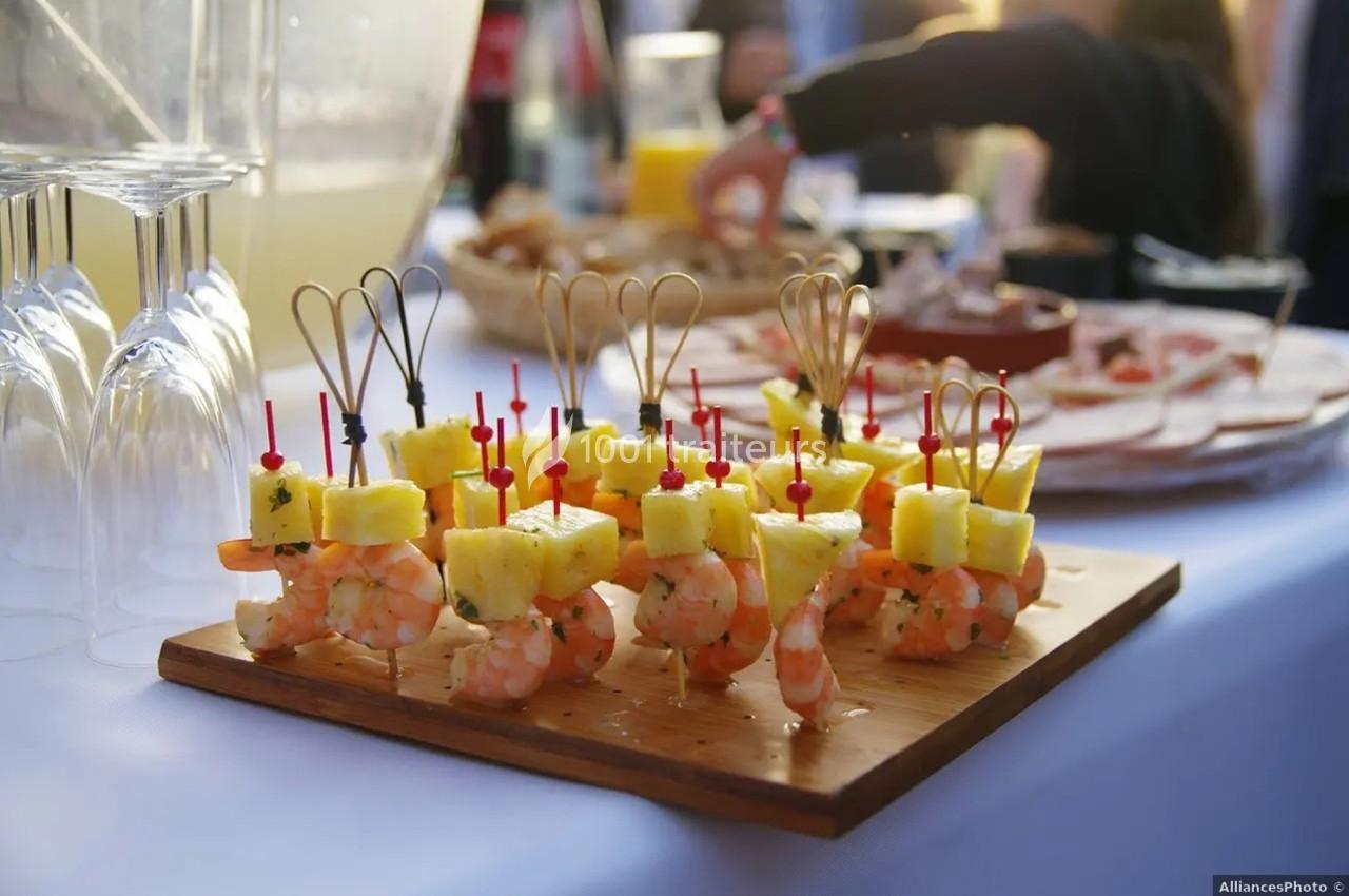Brochettes apéritives composées de crevettes et morceaux d'ananas, présentées sur une planche en bois.