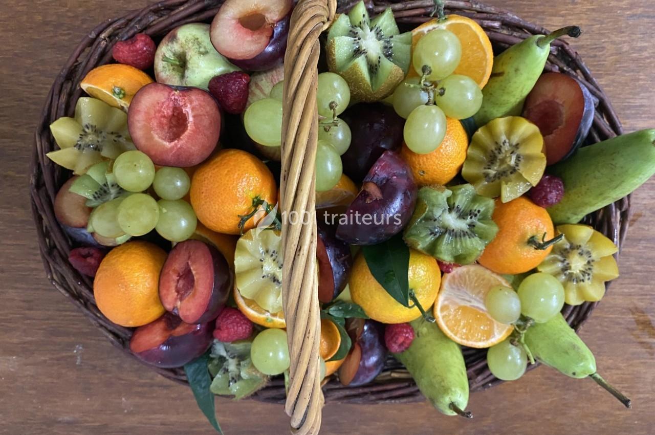 Panier en osier rempli de fruits variés, dont raisins, oranges, kiwis, prunes, poires et framboises, posé sur une table en…