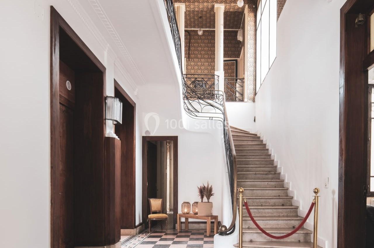 Escalier en marbre avec rampe en métal, entouré de murs blancs et de portes en bois sombre dans un intérieur lumineux.