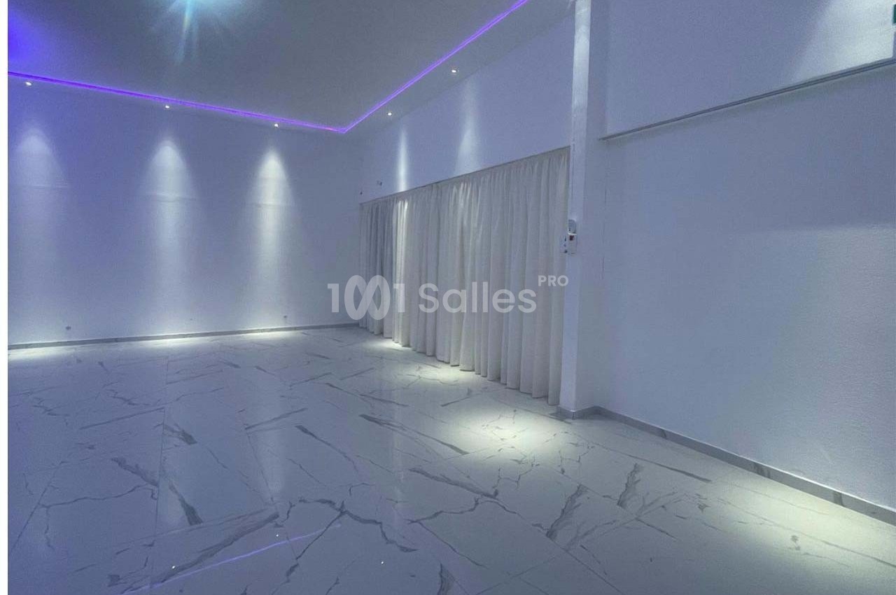 Salle vide avec sol en marbre clair, murs blancs, rideaux fermés et éclairage LED violet au plafond.