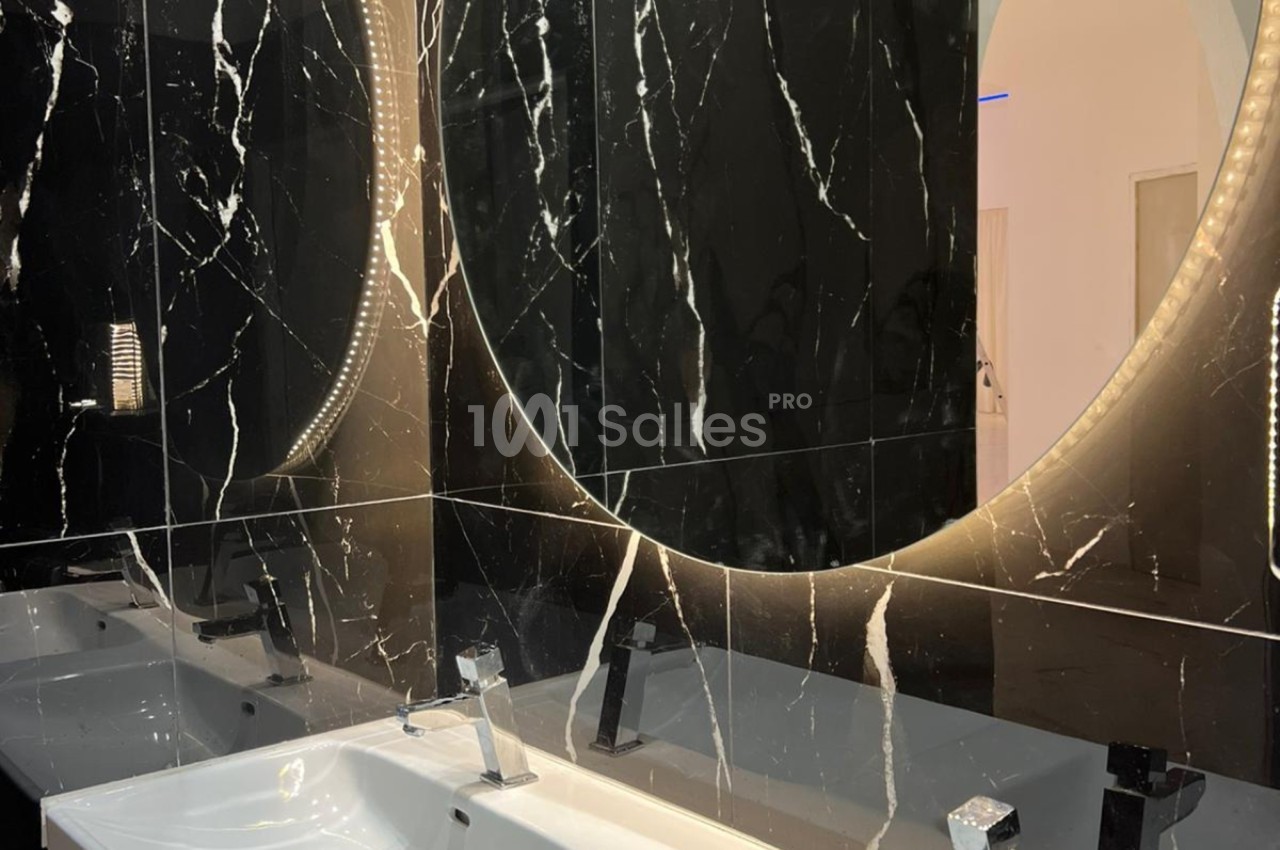 Lavabos modernes avec miroirs ronds rétroéclairés, entourés de murs en marbre noir veiné de blanc.