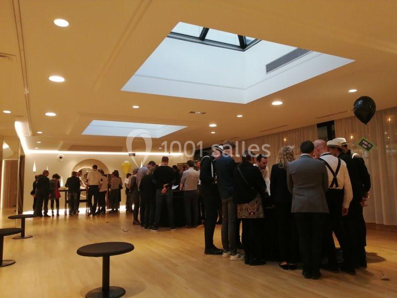 Des personnes debout en groupe discutent près de tables dans une salle lumineuse avec un plafond vitré.