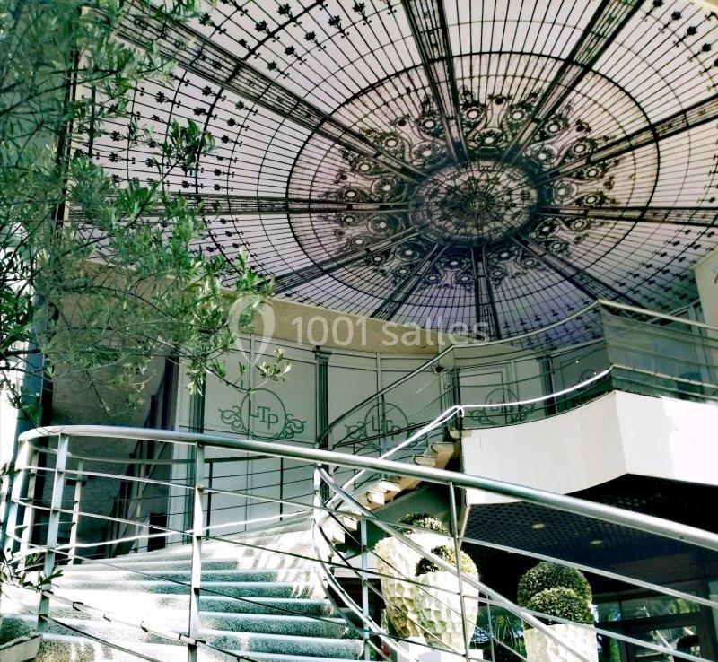 Escalier intérieur menant à une verrière décorative ornée de motifs complexes, entouré de plantes.