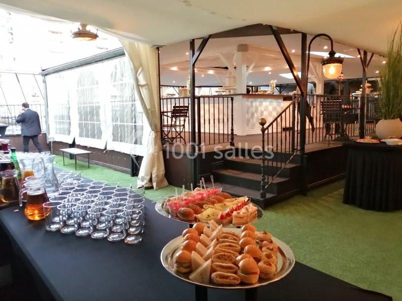 Buffet avec verrines, sandwichs et boissons disposés sous une tente, près d'une terrasse aménagée.