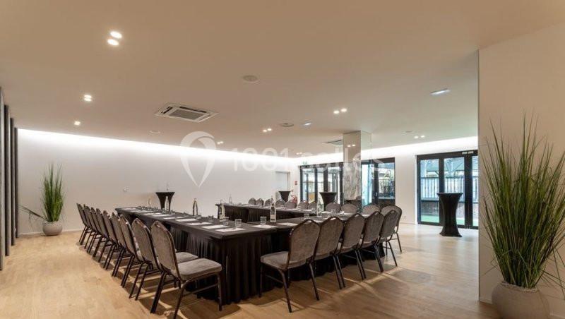 Salle de réunion lumineuse avec une grande table rectangulaire, des chaises alignées et des plantes décoratives.