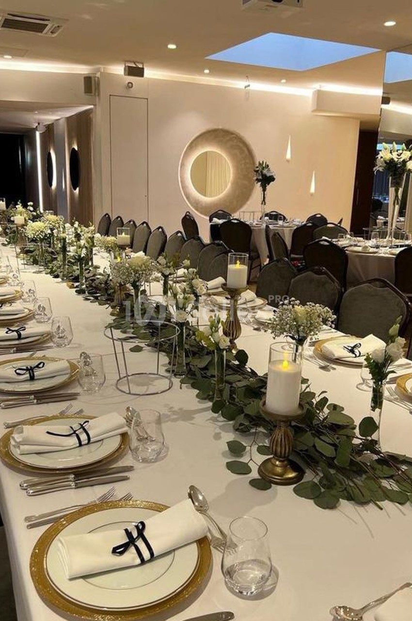 Table élégamment dressée pour un événement, avec nappes blanches, bougies, vaisselle raffinée et décoration florale.