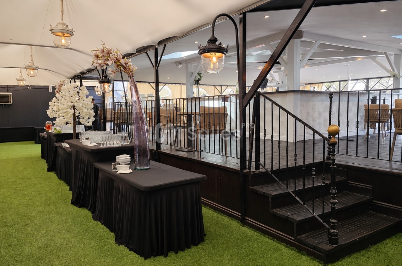 Salle événementielle avec tables drapées de noir, décor floral, escalier en bois et sol recouvert de gazon synthétique.