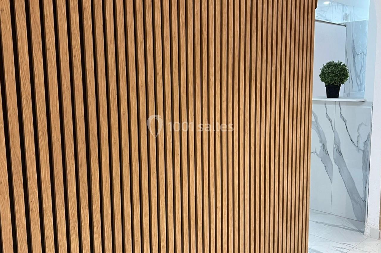 Panneau en bois à lattes verticales devant un espace intérieur avec mur en marbre et plante décorative.