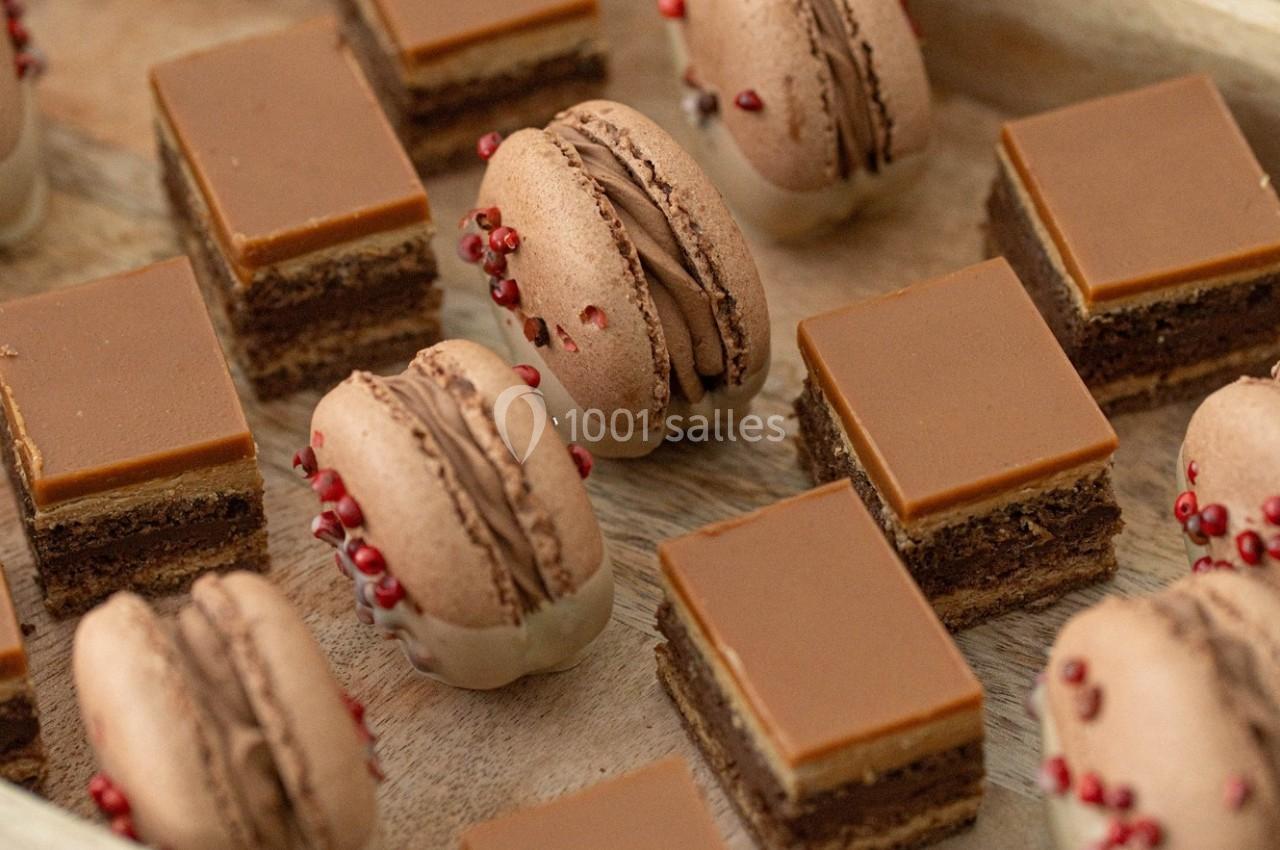 Assortiment de macarons au chocolat et de petits gâteaux carrés avec glaçage chocolaté sur un plateau en bois.