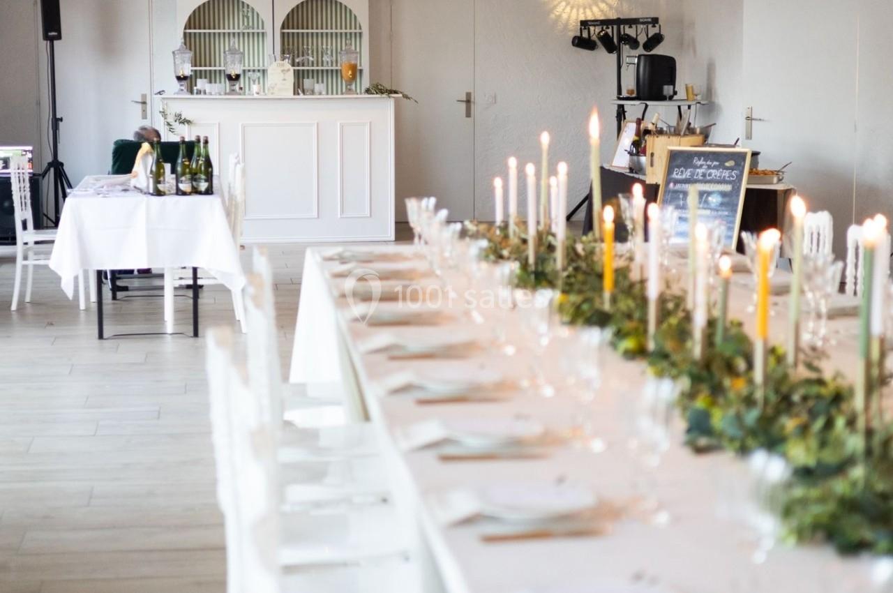 Grande table décorée avec des bougies et de la verdure dans une salle lumineuse avec un bar en arrière-plan.