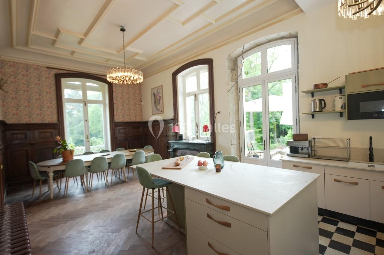 Cuisine spacieuse avec îlot central, grandes fenêtres, table à manger et vue sur un jardin verdoyant.