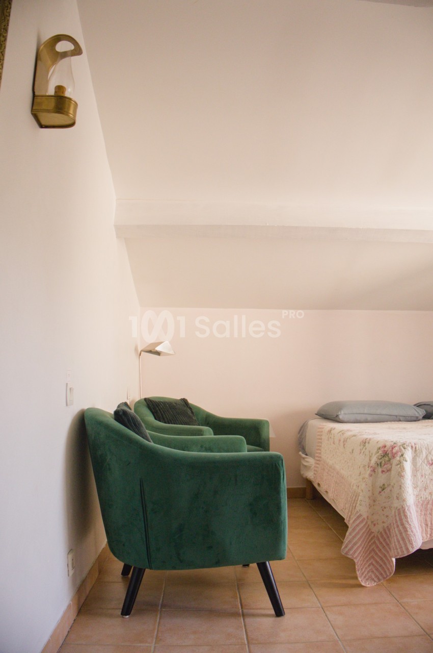 Fauteuil vert et lampe murale dans une chambre lumineuse avec un lit à motif floral.