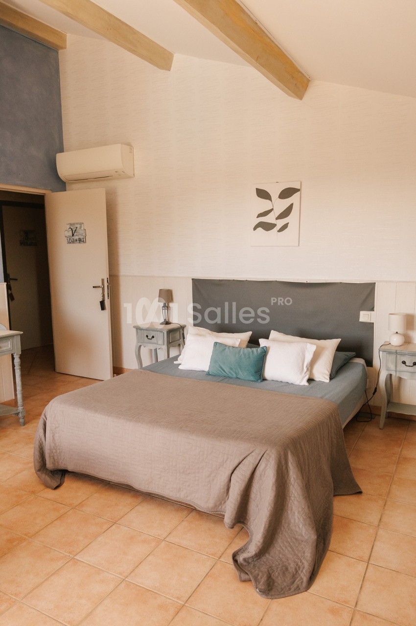 Chambre lumineuse avec lit double, couvre-lit beige, coussins décoratifs et mobilier en bois clair.