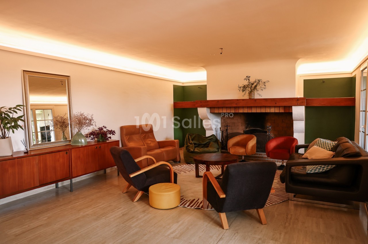 Salon chaleureux avec cheminée, mobilier vintage, fauteuils colorés, tapis rayé et buffet en bois.