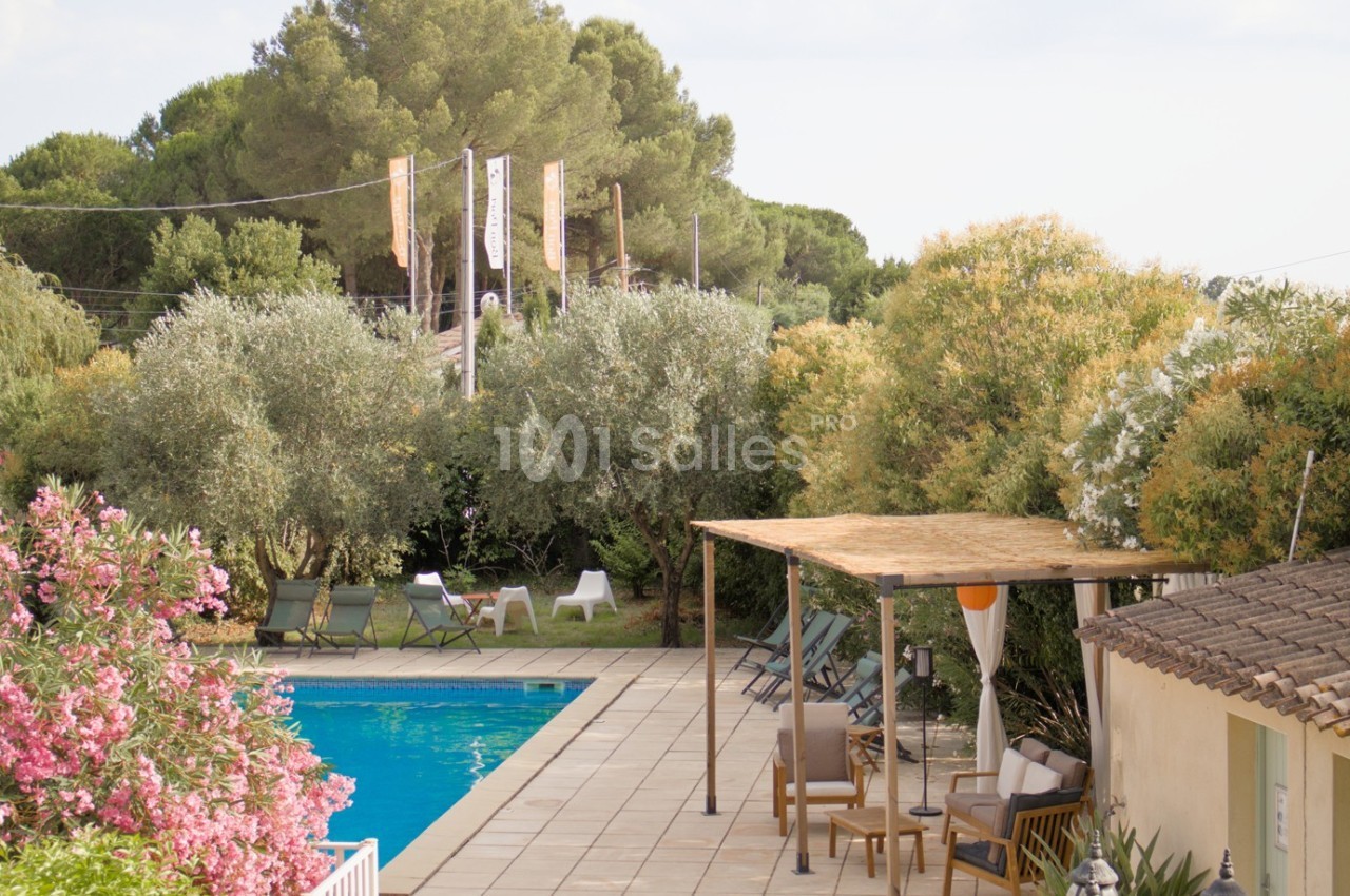Piscine extérieure entourée de végétation méditerranéenne, avec terrasse ombragée et chaises longues.