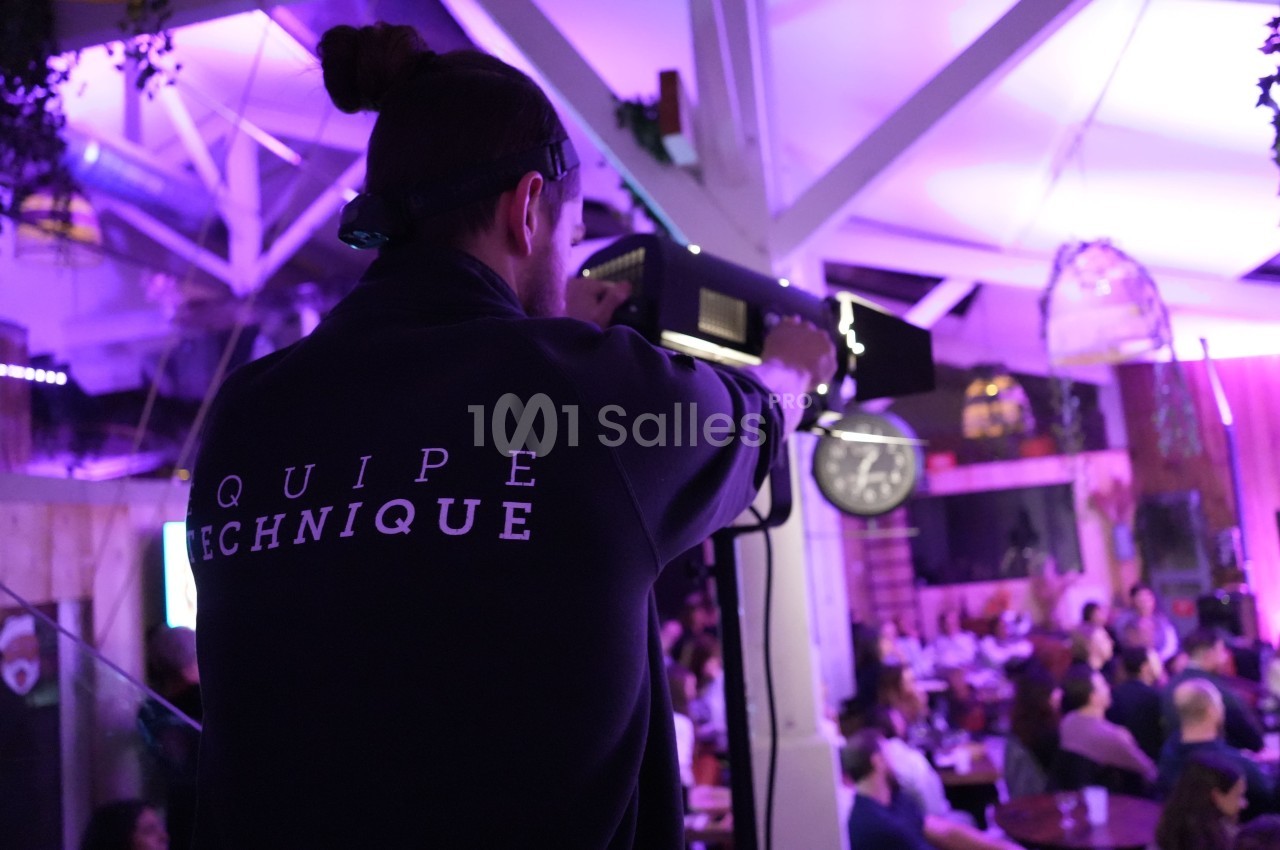 Un technicien ajuste un projecteur dans un espace intérieur éclairé, avec un public en arrière-plan.
